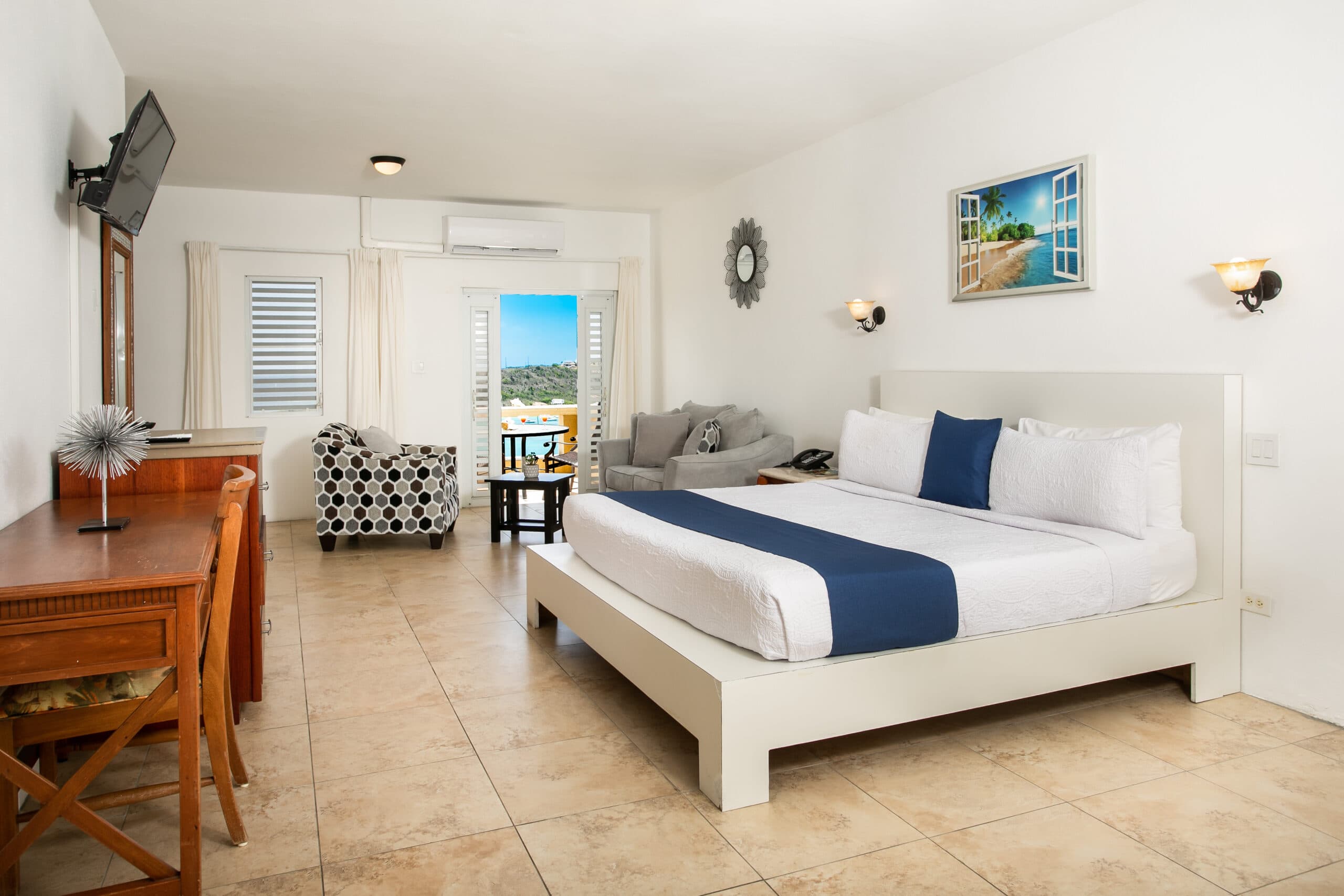 A modern hotel room featuring a king-sized bed, seating area, and a view of the outdoors through large windows.