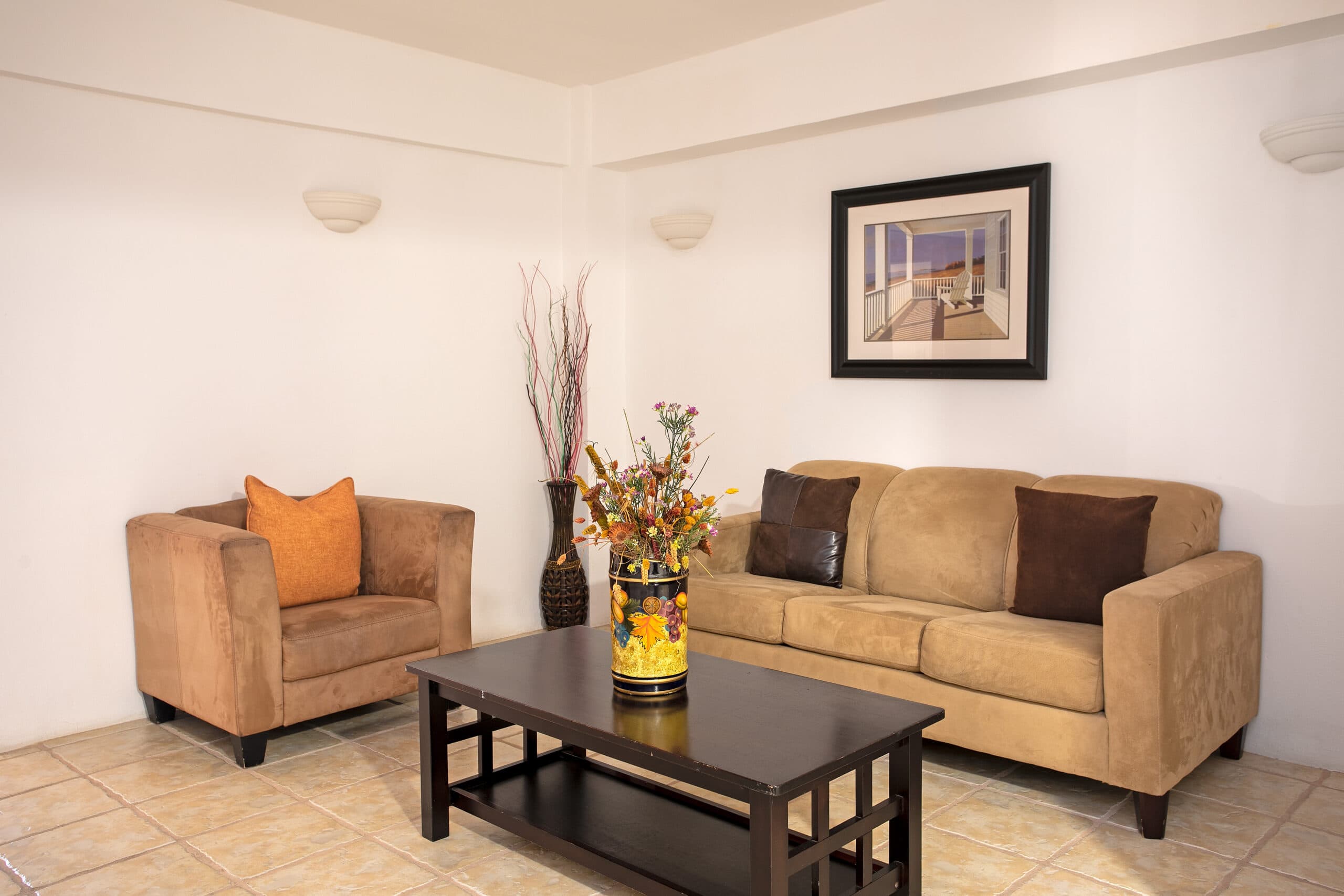 A cozy living room featuring a brown sofa, an armchair, a coffee table, and decorative flowers in a vase.