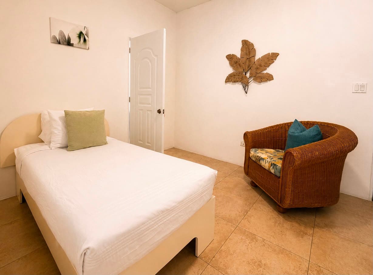 A simple bedroom featuring a single bed, a wicker chair, and decorative wall art.