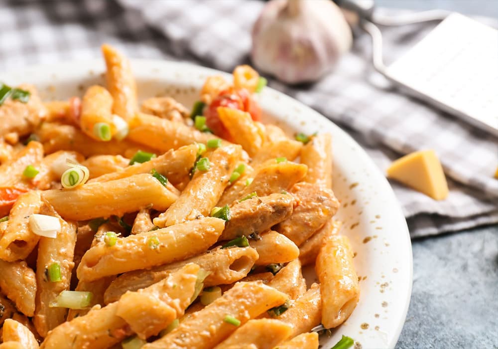 A plate of creamy pasta with chicken, topped with green onions and accompanied by garlic and cheese.
