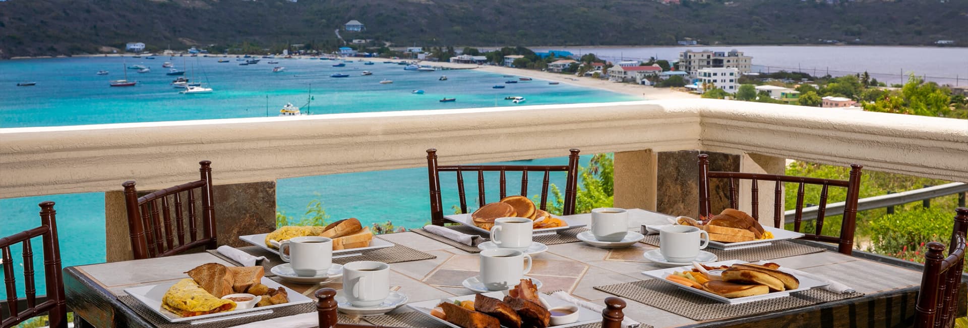 A beautifully set breakfast table with plates and cups overlooks a serene waterfront view.