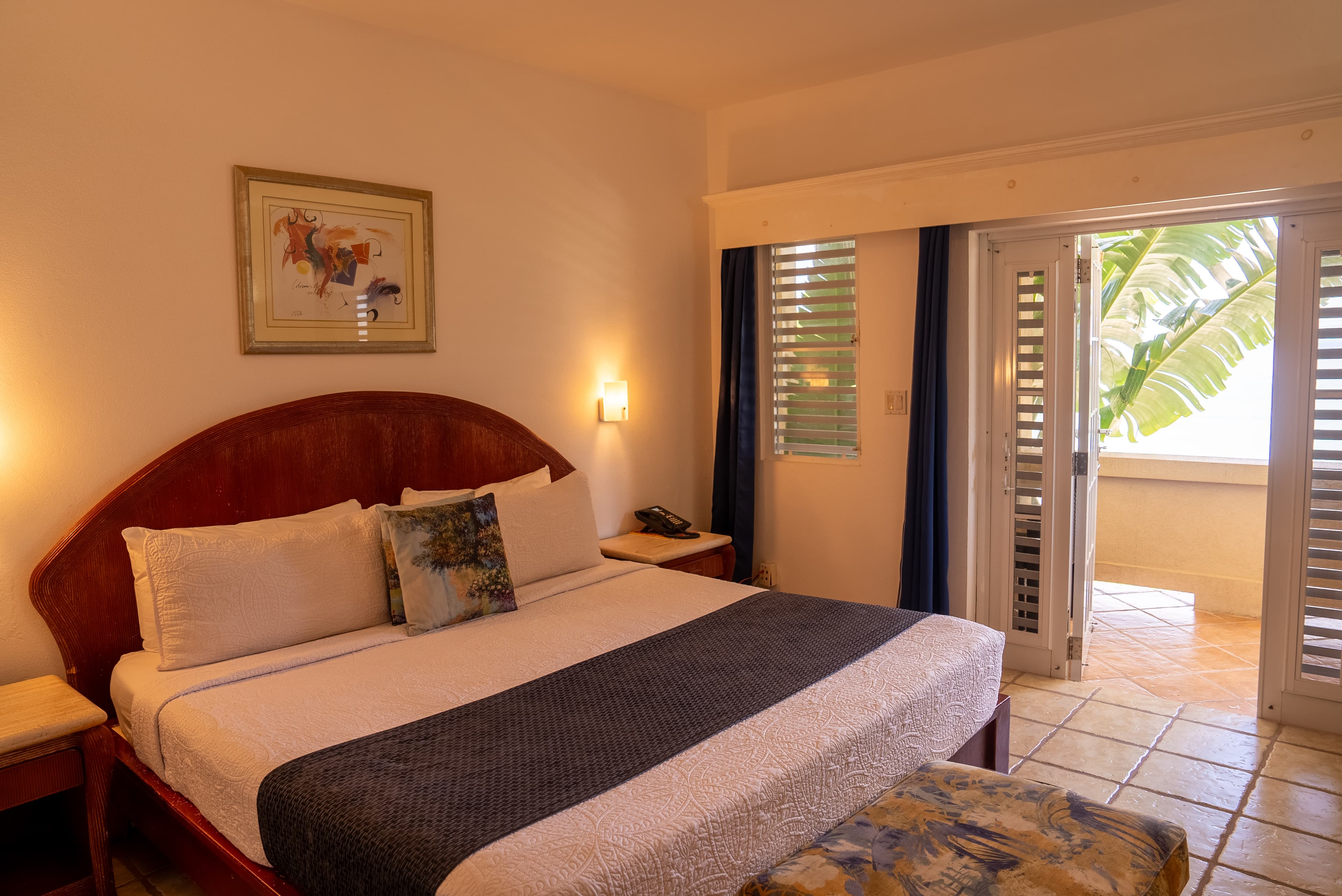 A cozy hotel room featuring a large bed and sliding doors leading to a balcony with tropical views.