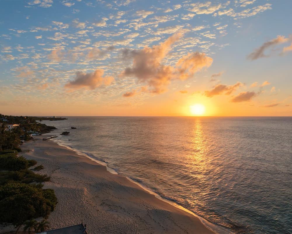 A serene beach at sunset with golden hues reflecting on the water and scattered clouds in the sky.