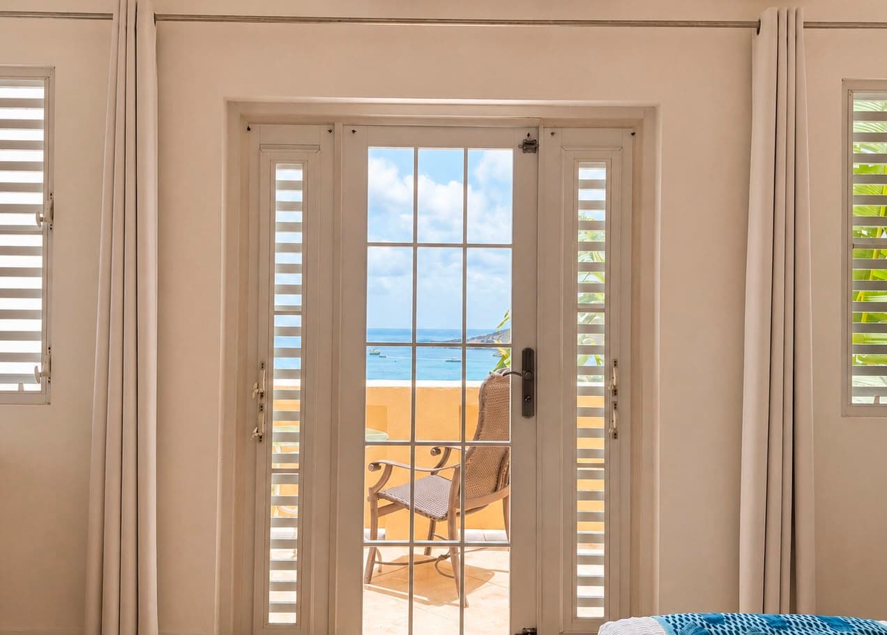 A view of the ocean through double glass doors, framed by white curtains.