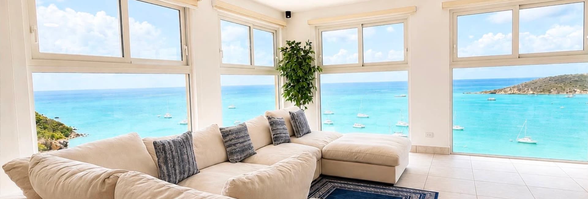 A bright, airy living room features a large white sectional sofa and panoramic ocean views through expansive windows.