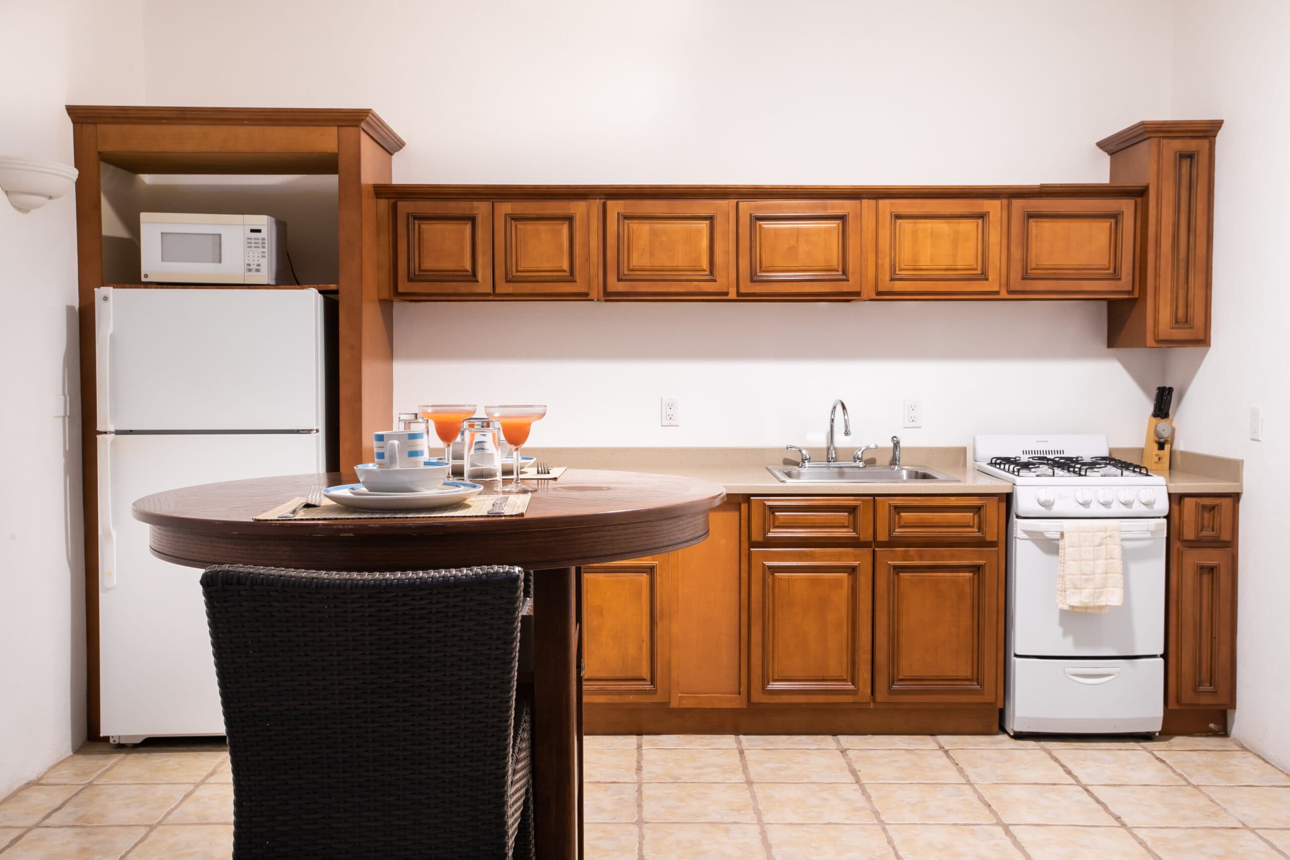 A modern kitchen featuring wooden cabinets, a round table set with dishware, and a white refrigerator.