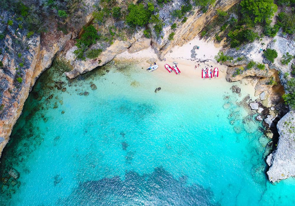 Aerial view of a secluded beach with turquoise waters and a group of people near the shore.