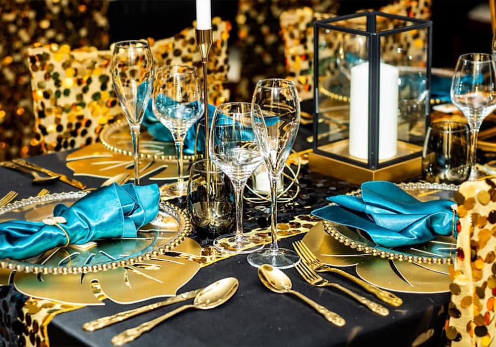 Elegant dining table set with gold utensils, teal napkins, and sparkling decorations.