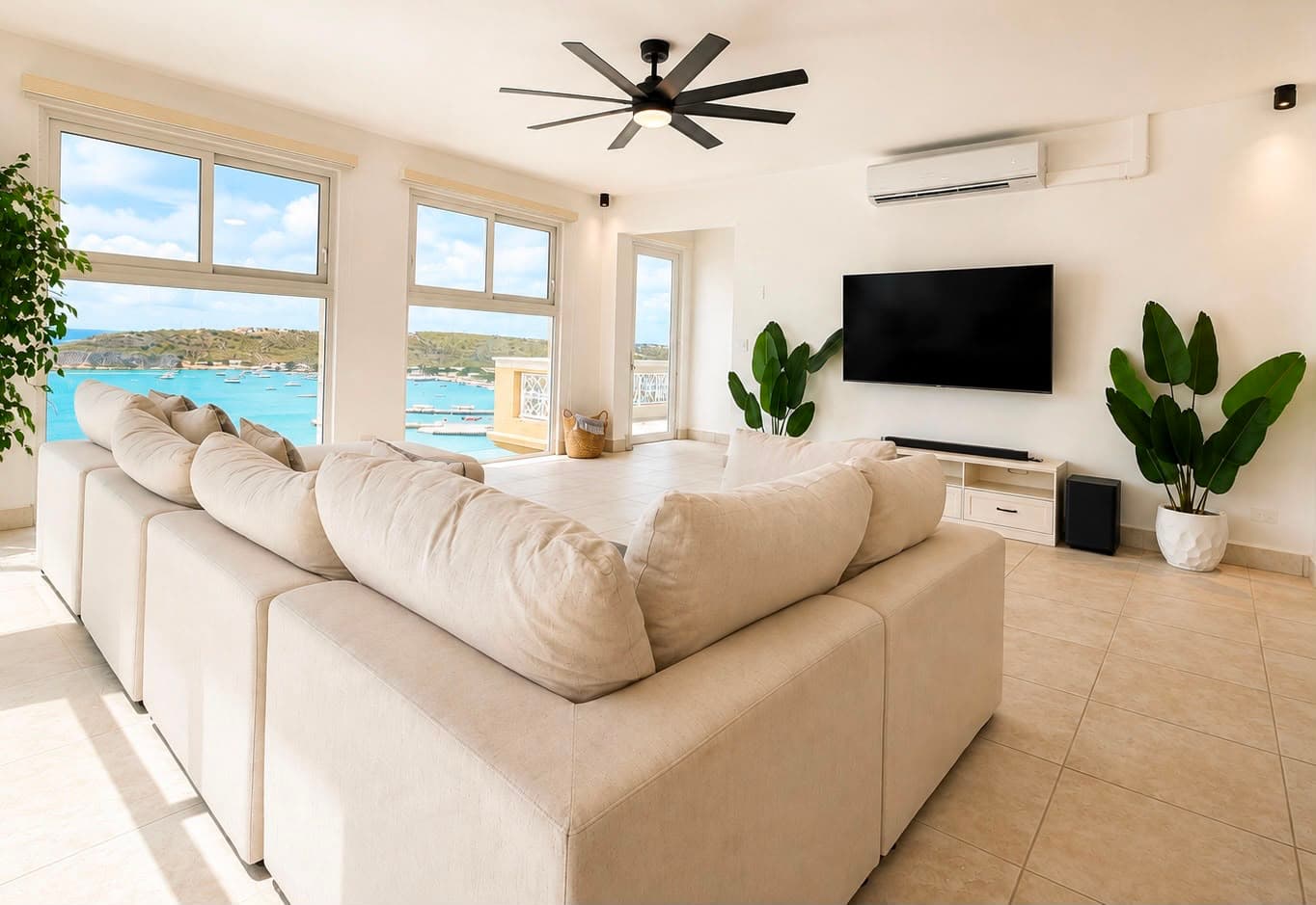 Bright, spacious living room with a large cream sofa, a view of the ocean, and indoor plants.