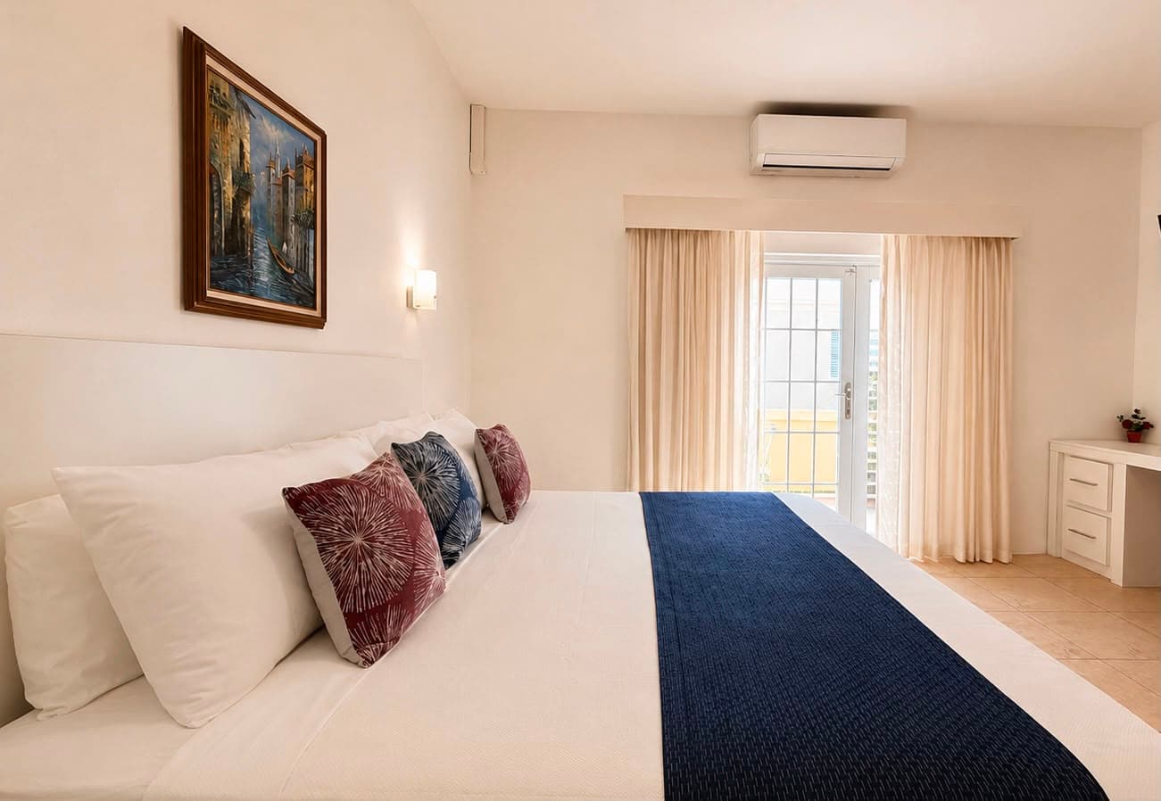 A modern bedroom with a large bed, decorative pillows, a painting on the wall, and natural light coming through the curtains.