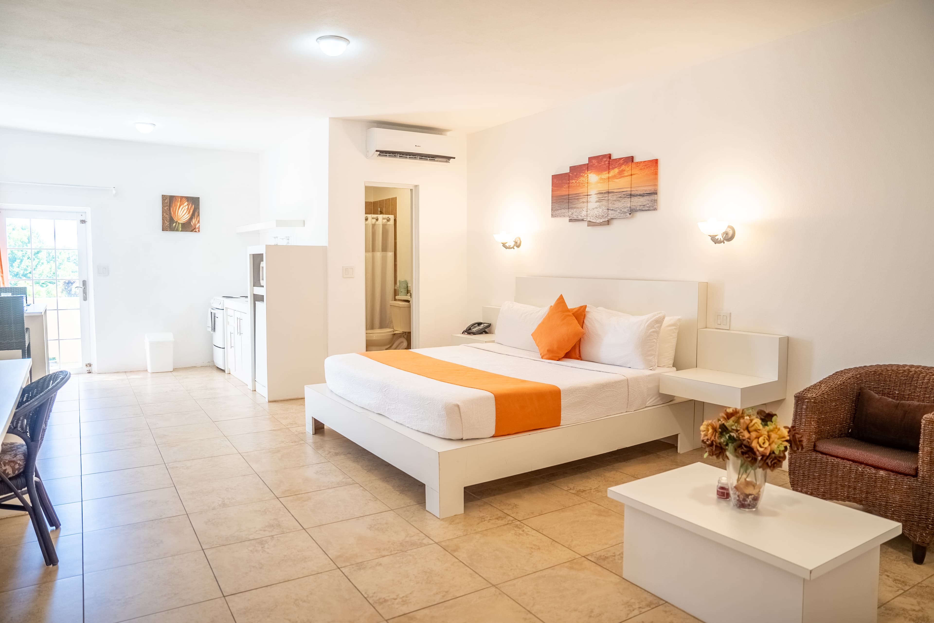 Bright and modern hotel room with a queen bed, kitchenette, and warm decor.