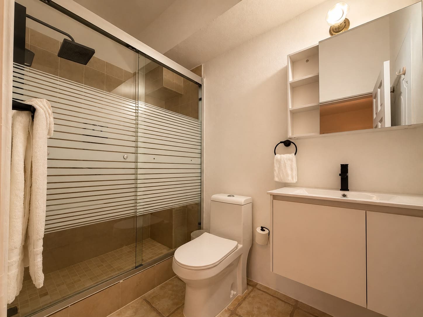 A modern bathroom featuring a glass shower, toilet, and vanity with a mirror.
