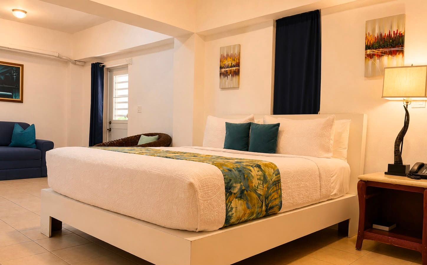 A cozy hotel room featuring a queen-sized bed, decorative pillows, and a small seating area.