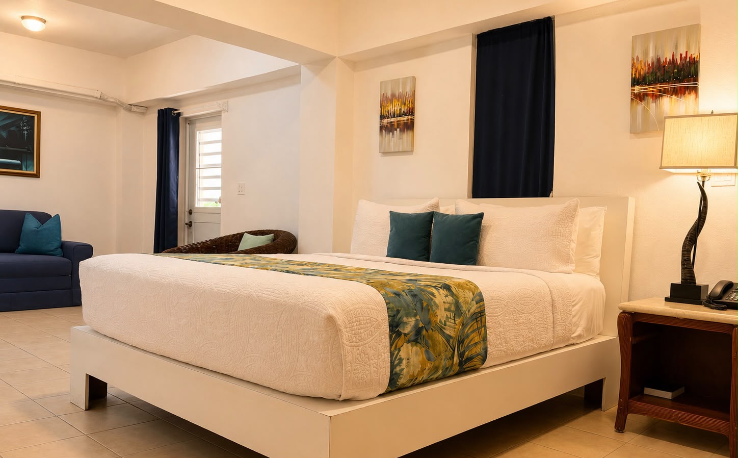 A cozy hotel room featuring a queen-sized bed, decorative pillows, and a small seating area.