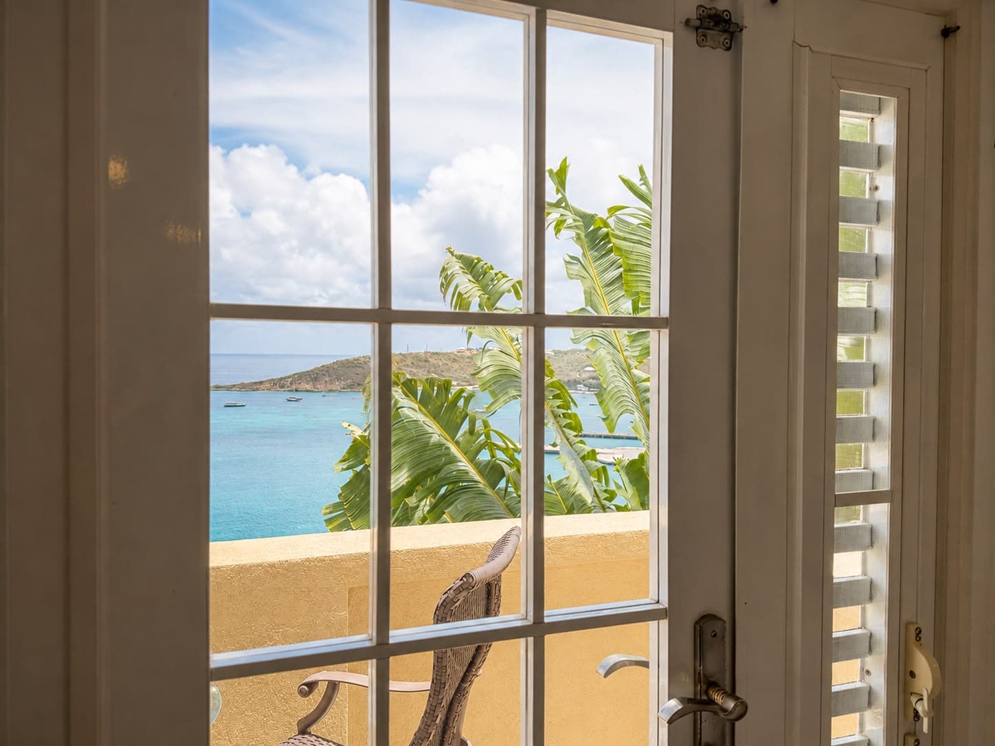 View of a tropical seascape through a window with a palm frond in the foreground.
