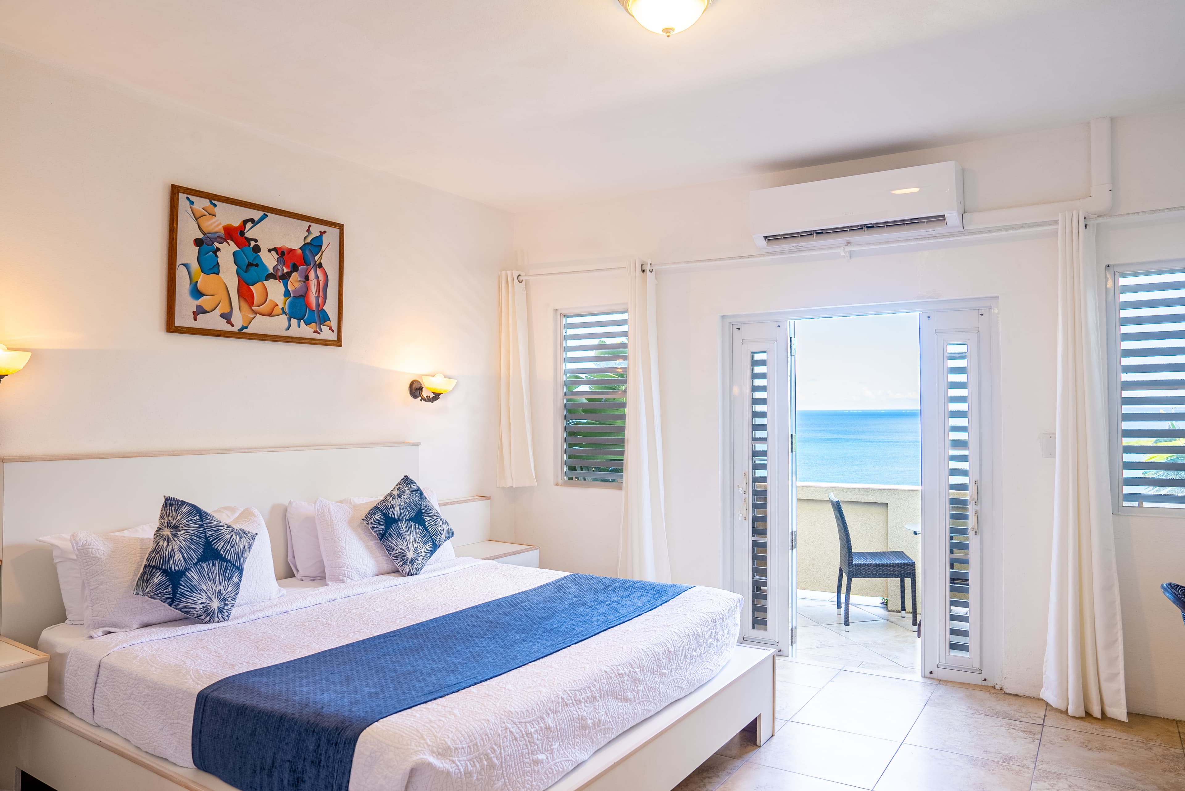 A bright, beachfront hotel room with a king-size bed and large windows showcasing ocean views.