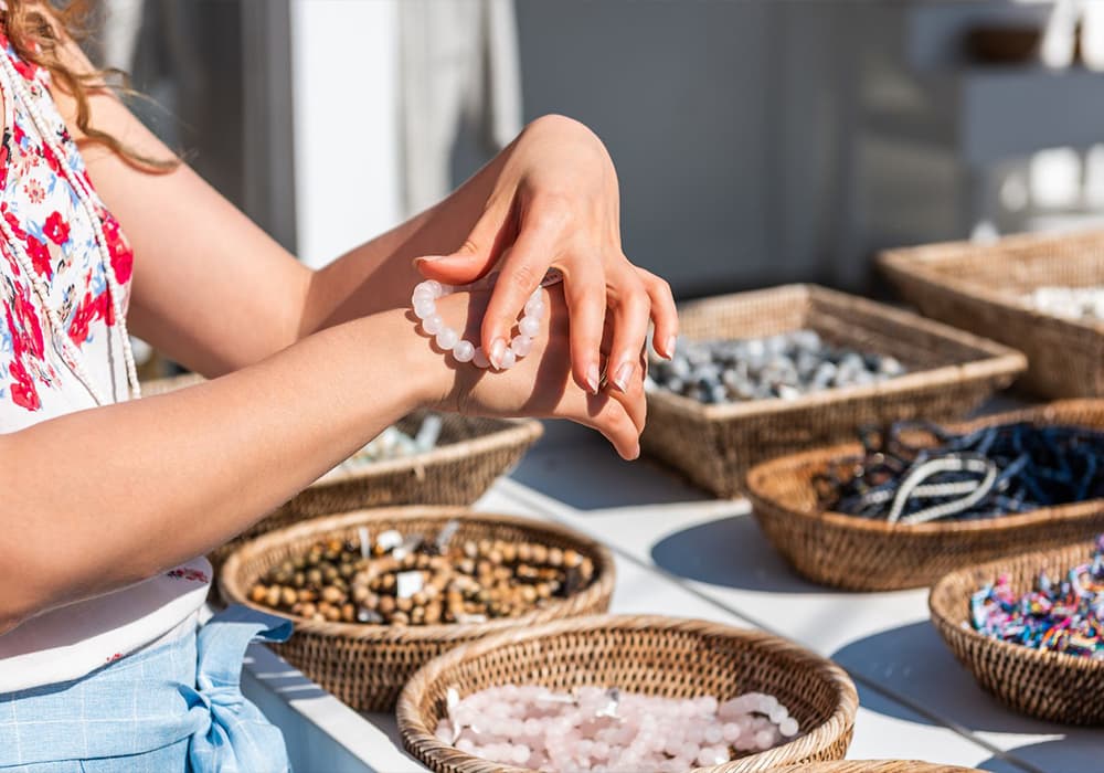 A person tries on a bracelet while surrounded by various beaded jewelry in woven baskets.