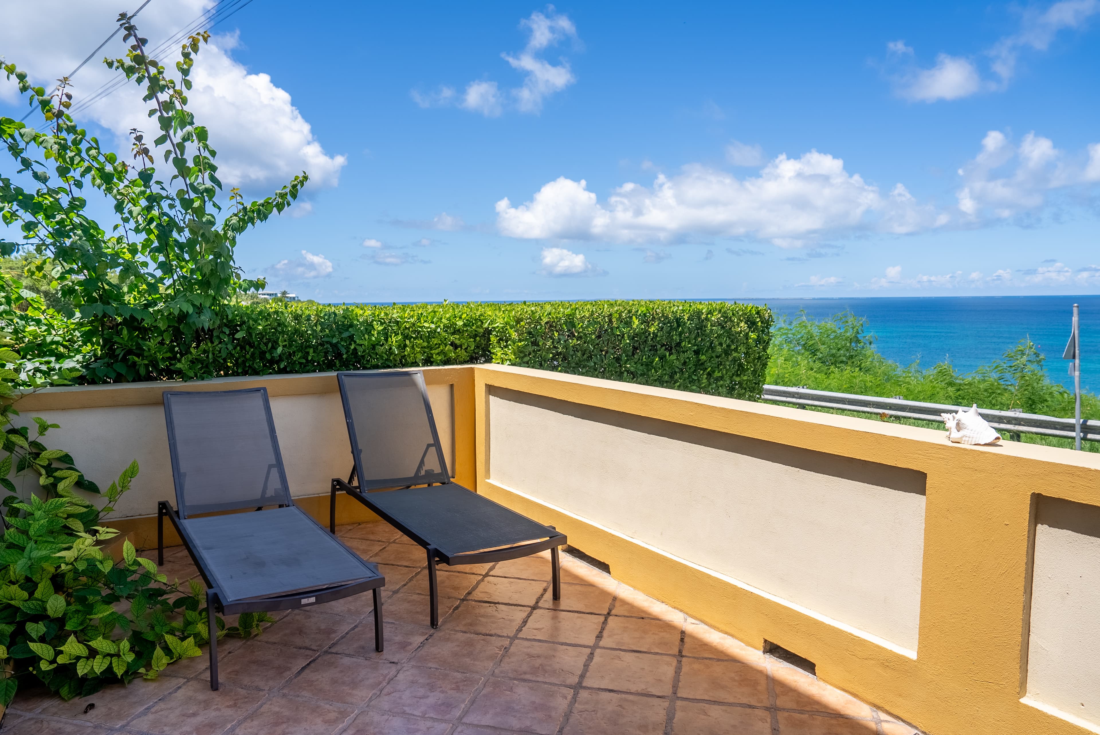 A terrace with two loungers overlooking a scenic ocean view and blue sky.