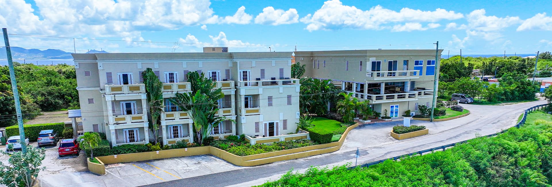 Aerial view of a hotel surrounded by greenery under a blue sky with clouds.