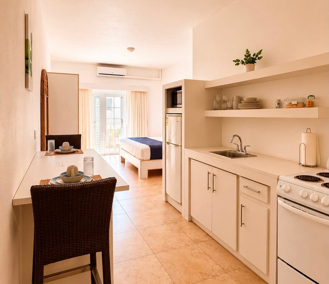 A modern, well-lit kitchen area with a dining table, refrigerator, and a view into a bedroom beyond.