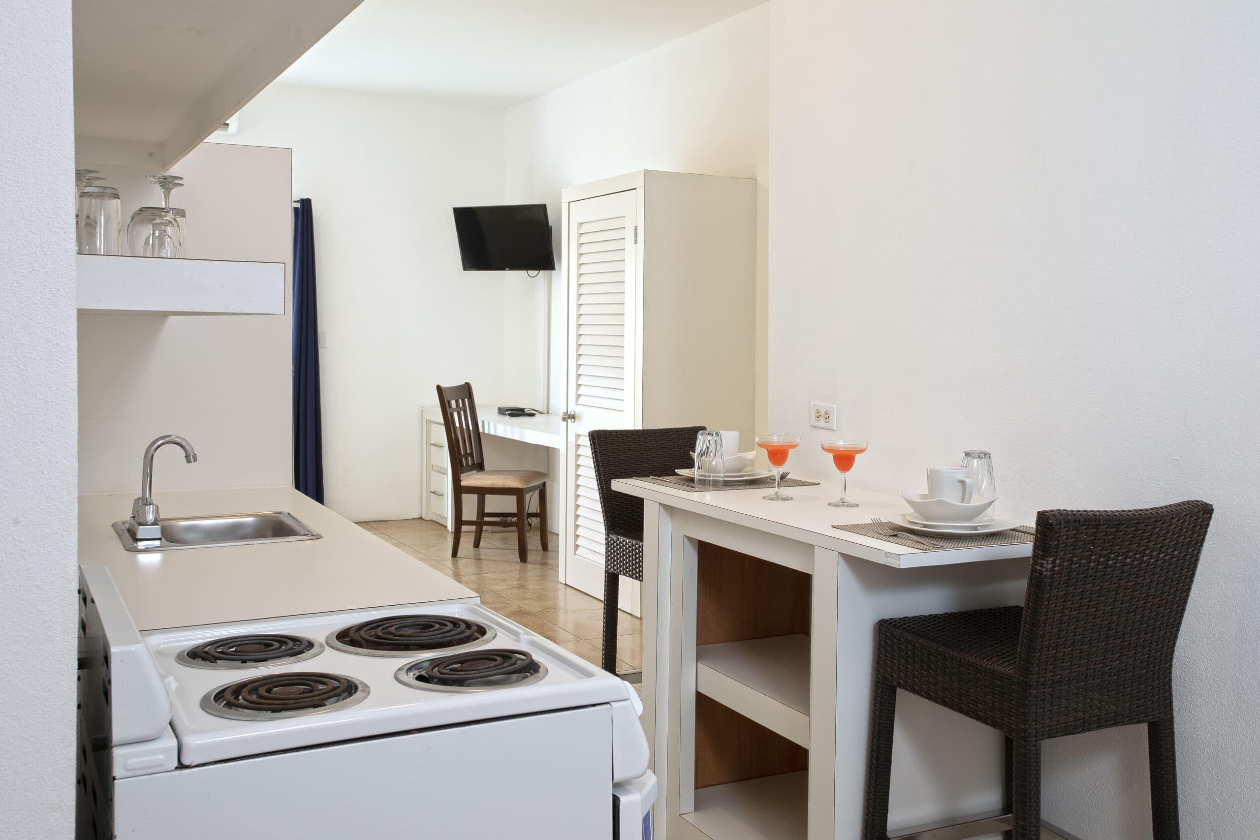A modern kitchenette and dining area featuring a stove, table for two, and a small workspace.