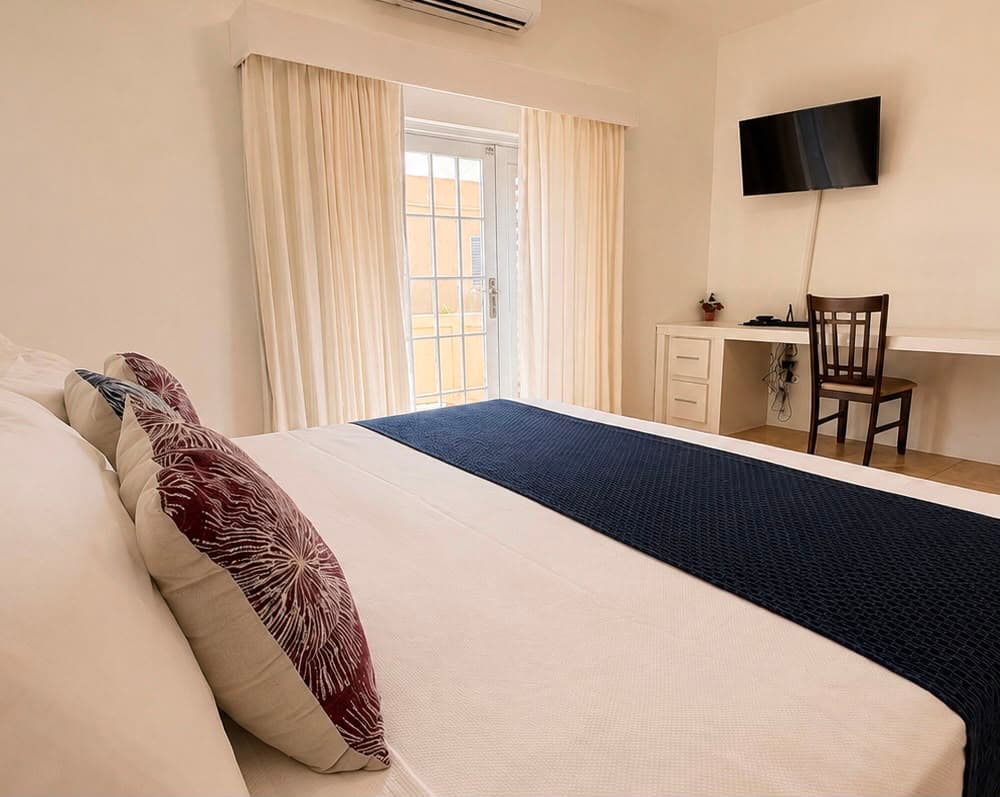 A cozy bedroom featuring a bed with decorative pillows, a desk, a chair, and a window with curtains.