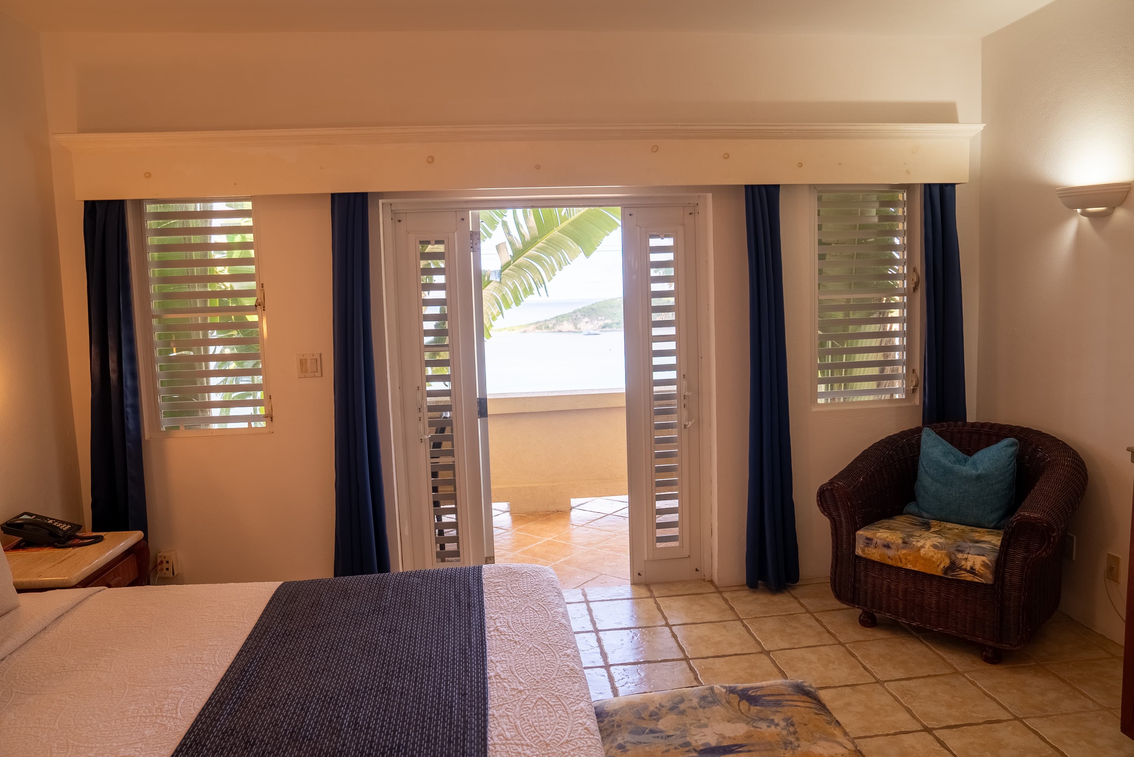 A cozy hotel room featuring a bed, decorative chair, and large doors leading to a balcony with views.