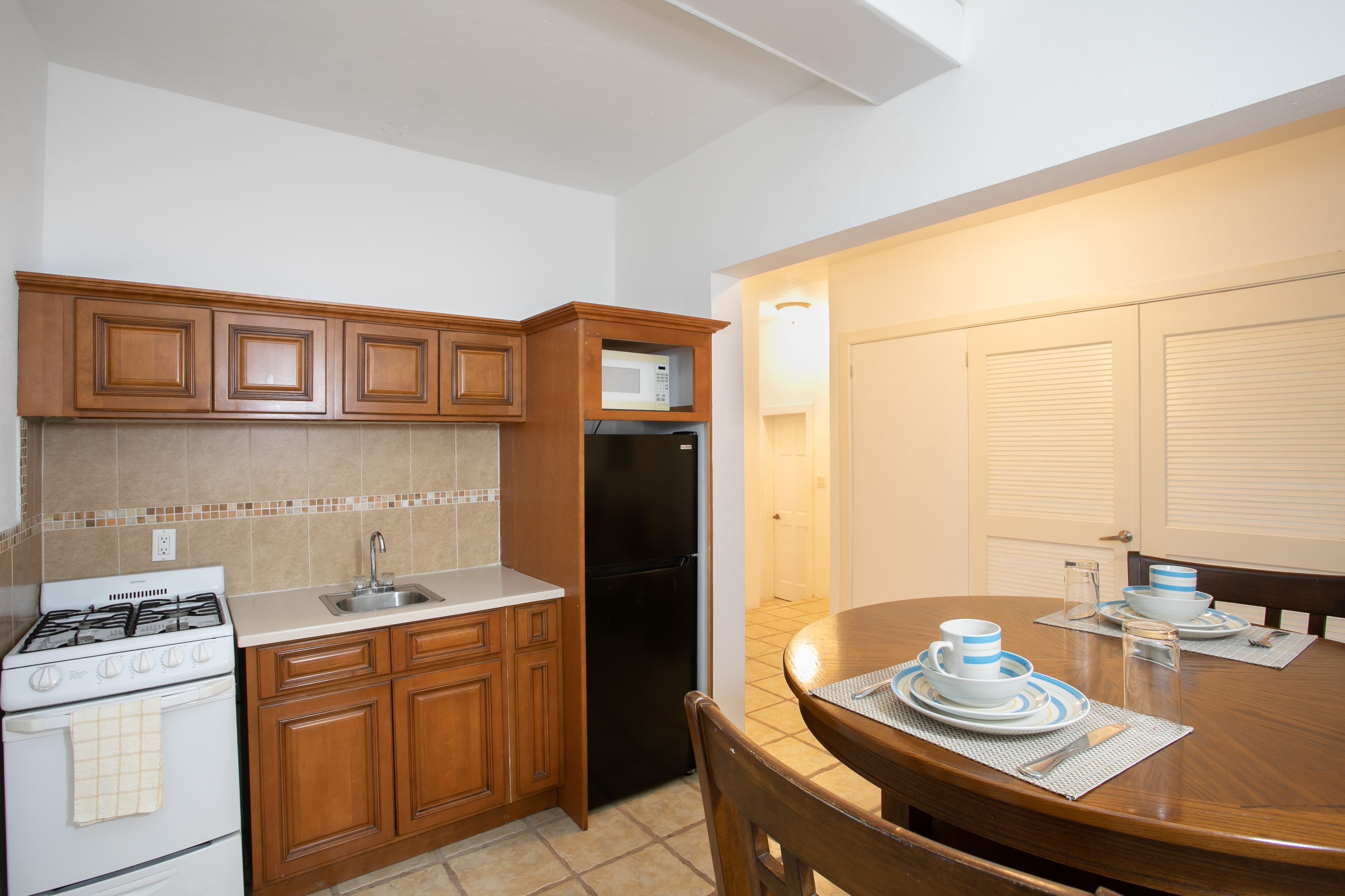 A compact kitchen with wooden cabinets, a gas stove, and a dining table set for two.