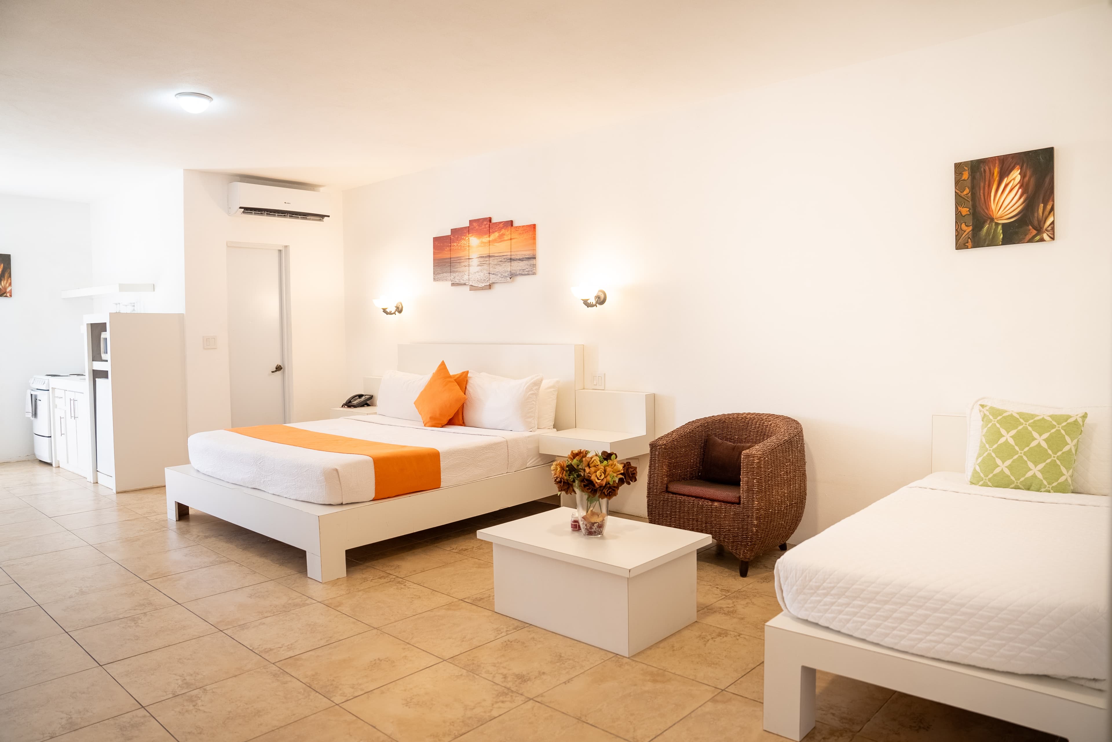 Bright hotel room featuring two beds, a small table, and a cozy chair.