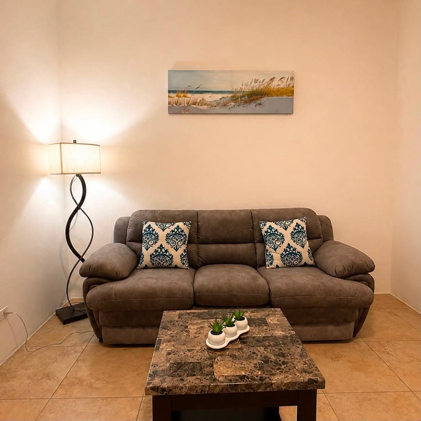 A cozy living room featuring a gray sofa with patterned cushions, a marble coffee table, and a lamp beside a wall art piece.