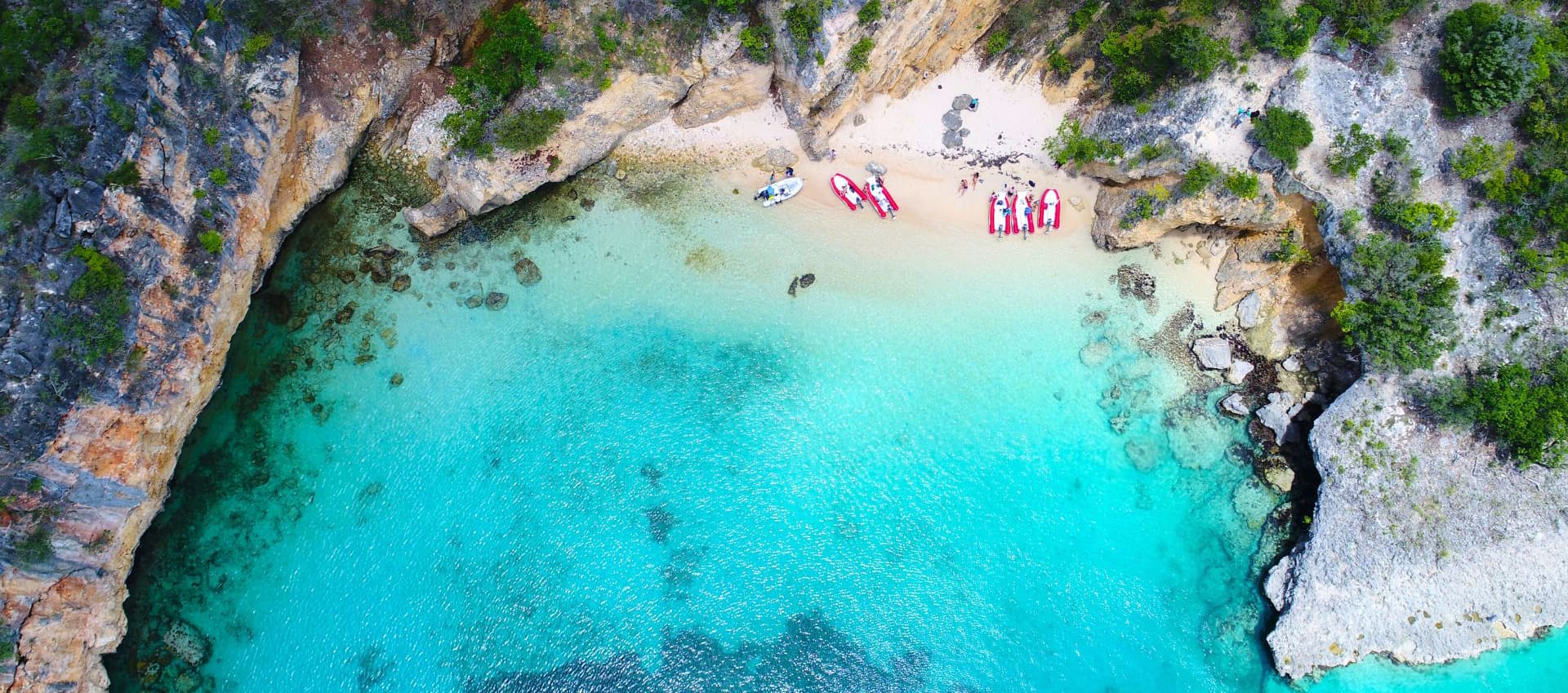 Aerial view of a secluded beach with turquoise water and people in kayaks near the shoreline.