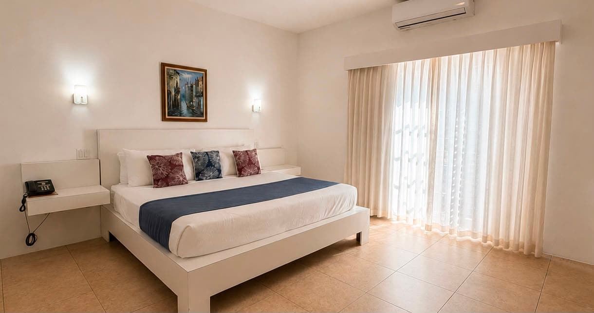 Bright and airy hotel room featuring a large bed, minimalist decor, and natural light from a window.