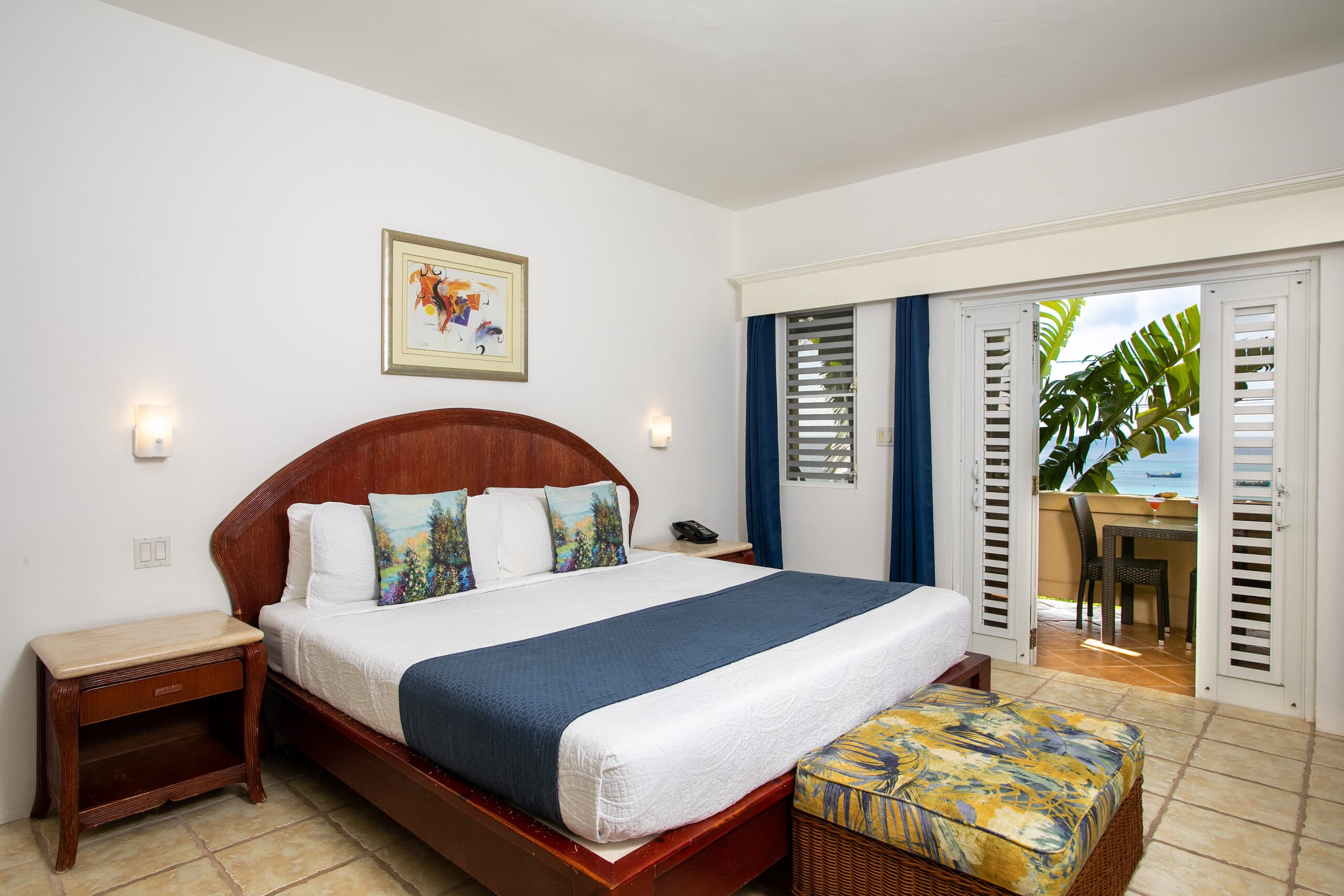 A cozy hotel room with a large bed, decorative pillows, and a view of a patio through sliding doors.