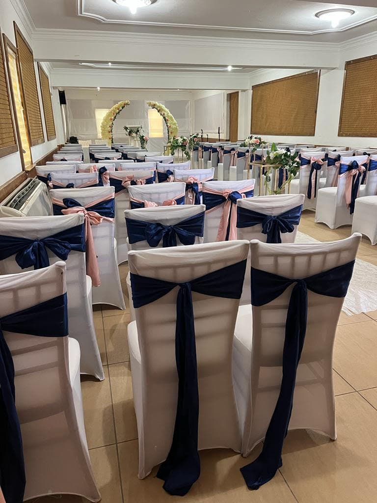 A wedding venue with rows of white chairs adorned with navy and pink sashes.