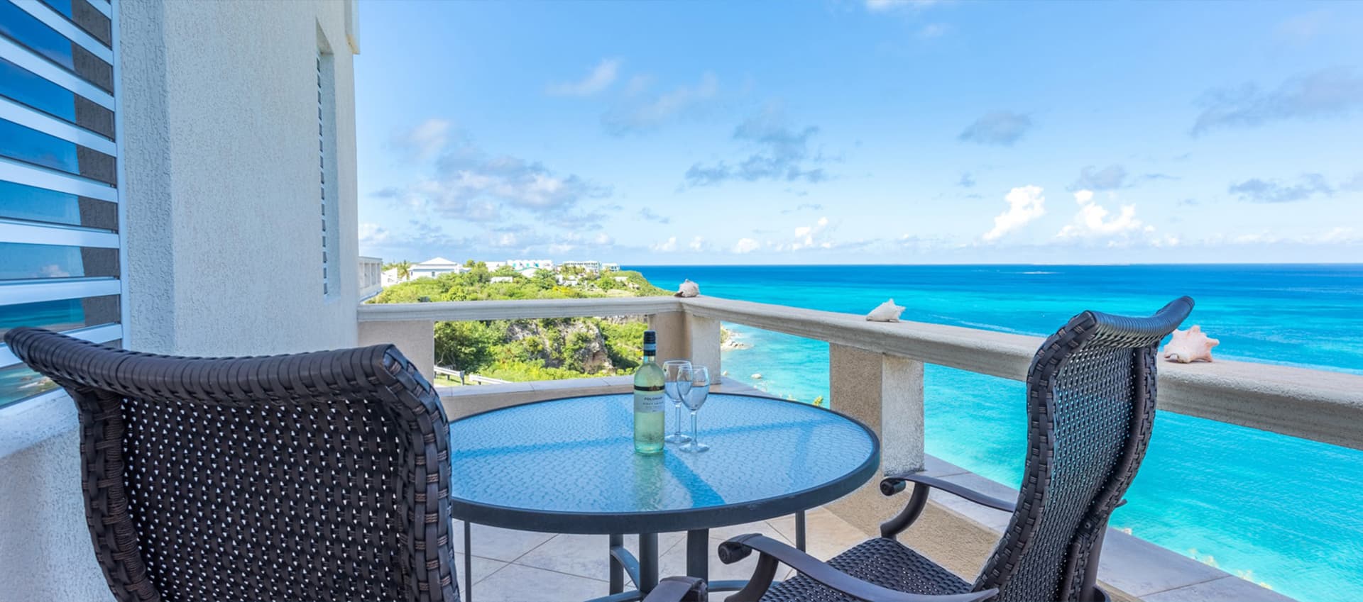 A balcony with a table and chairs overlooking a scenic view of the ocean and coastline.