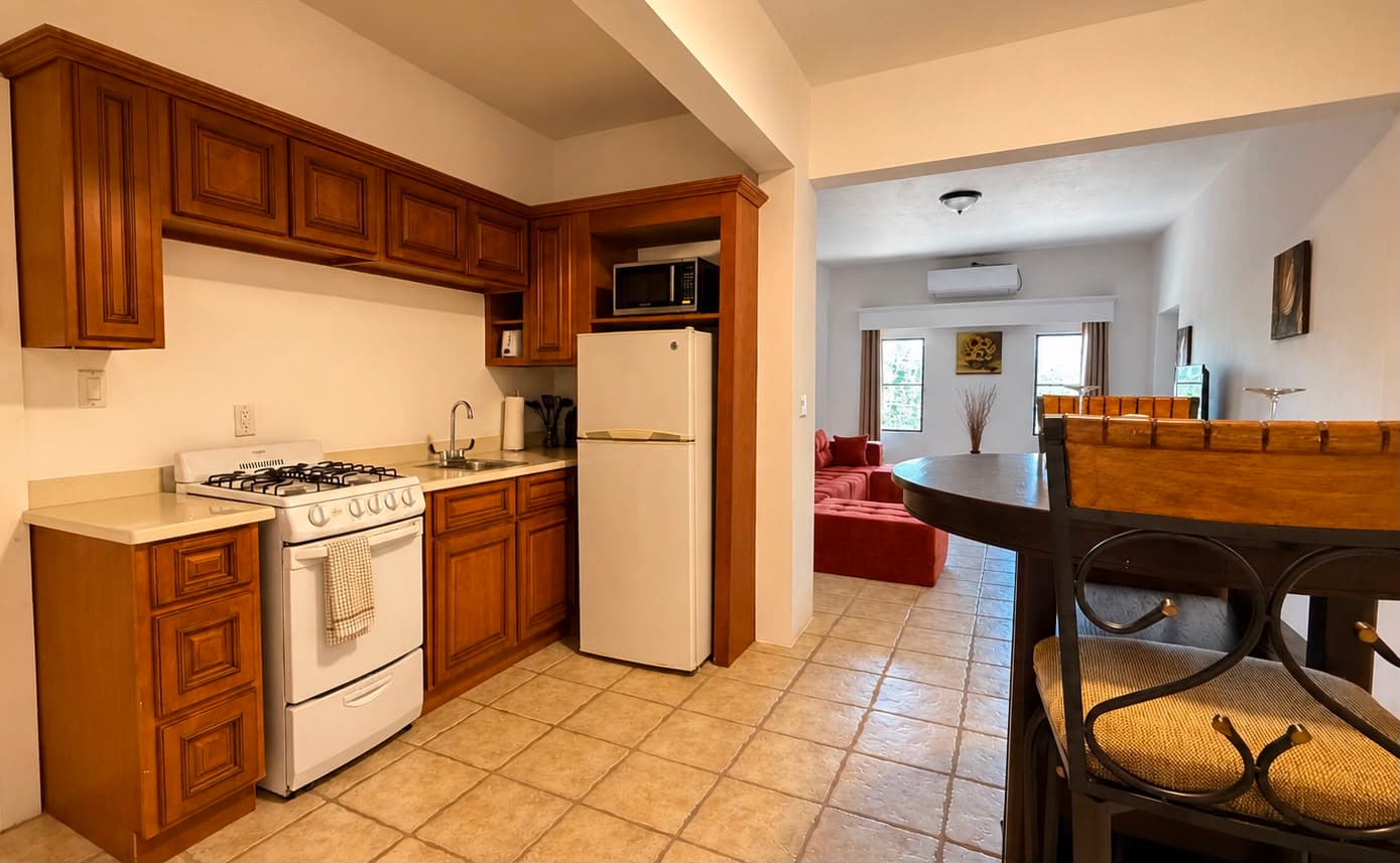 A cozy kitchen featuring wooden cabinets, a gas stove, and an open layout leading to a living area with a red sofa.