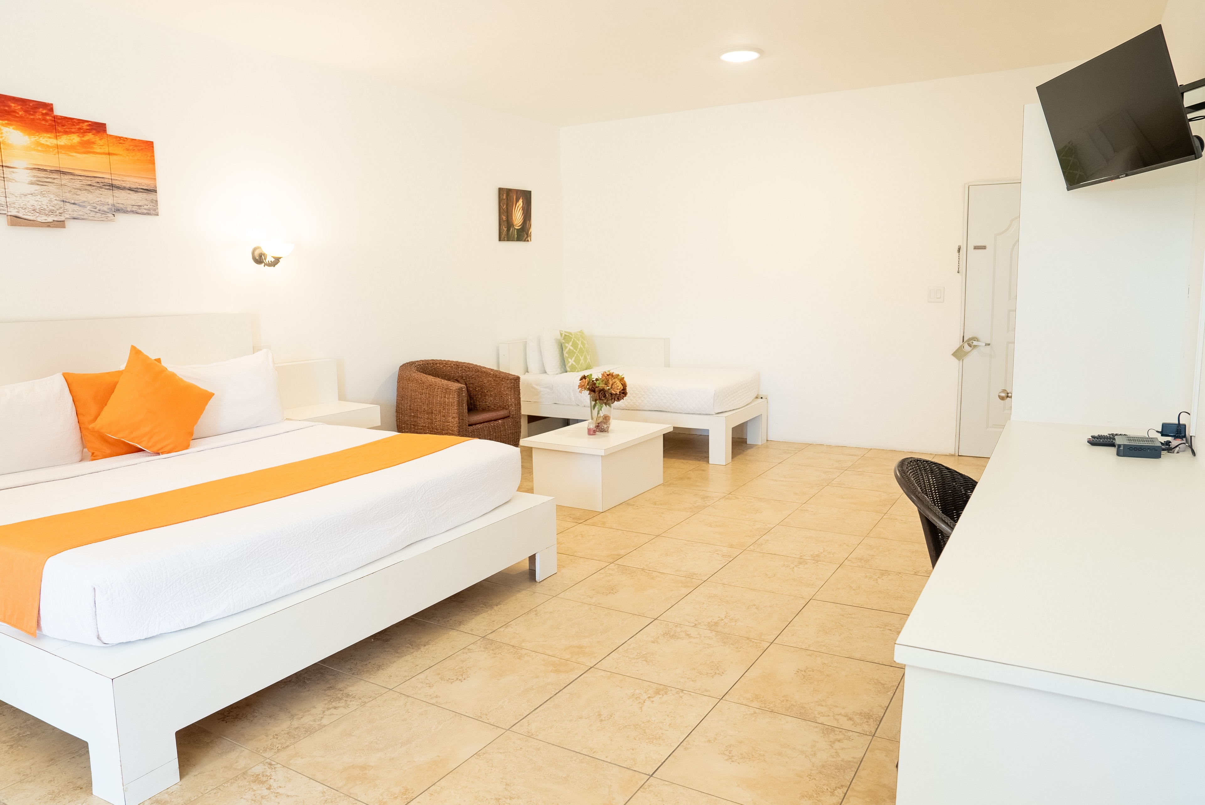 A bright, minimalistic hotel room featuring a queen bed, a seating area, and a workspace.