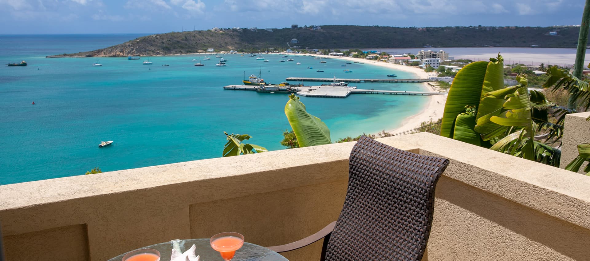View from a balcony overlooking a turquoise bay with boats and a beach.