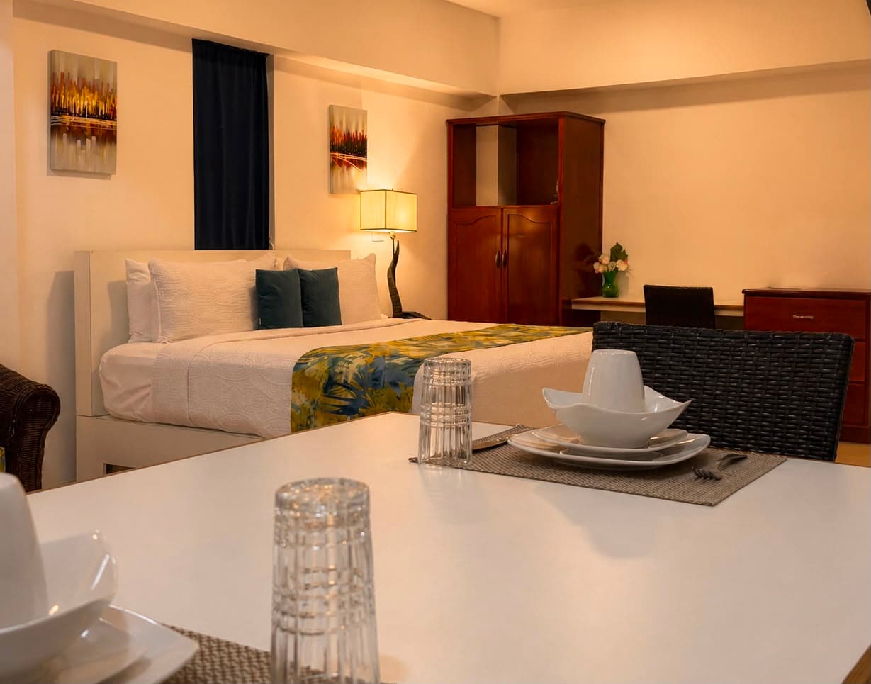 A cozy room featuring a bed with decorative pillows, a dining table set, and warm lighting.