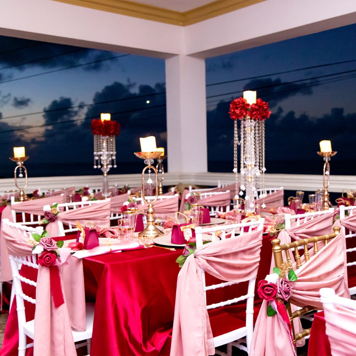 Elegant banquet setup with white chairs adorned in pink fabric and floral accents, against a twilight backdrop.