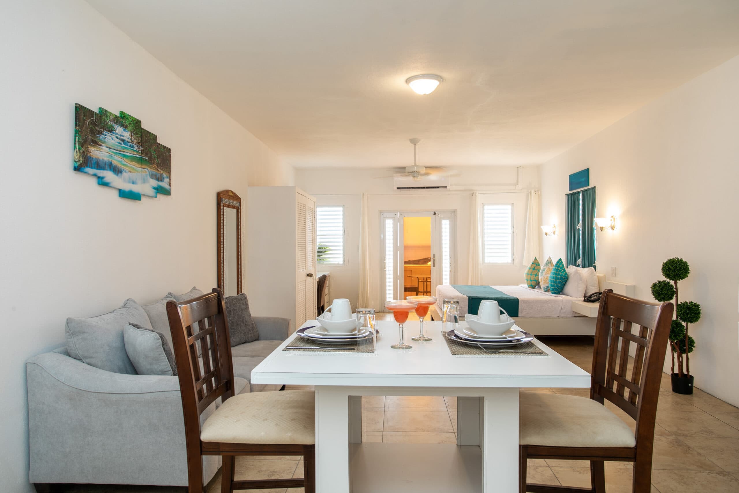 A bright and modern living space featuring a dining table, comfortable seating, and a clear view toward a bedroom.