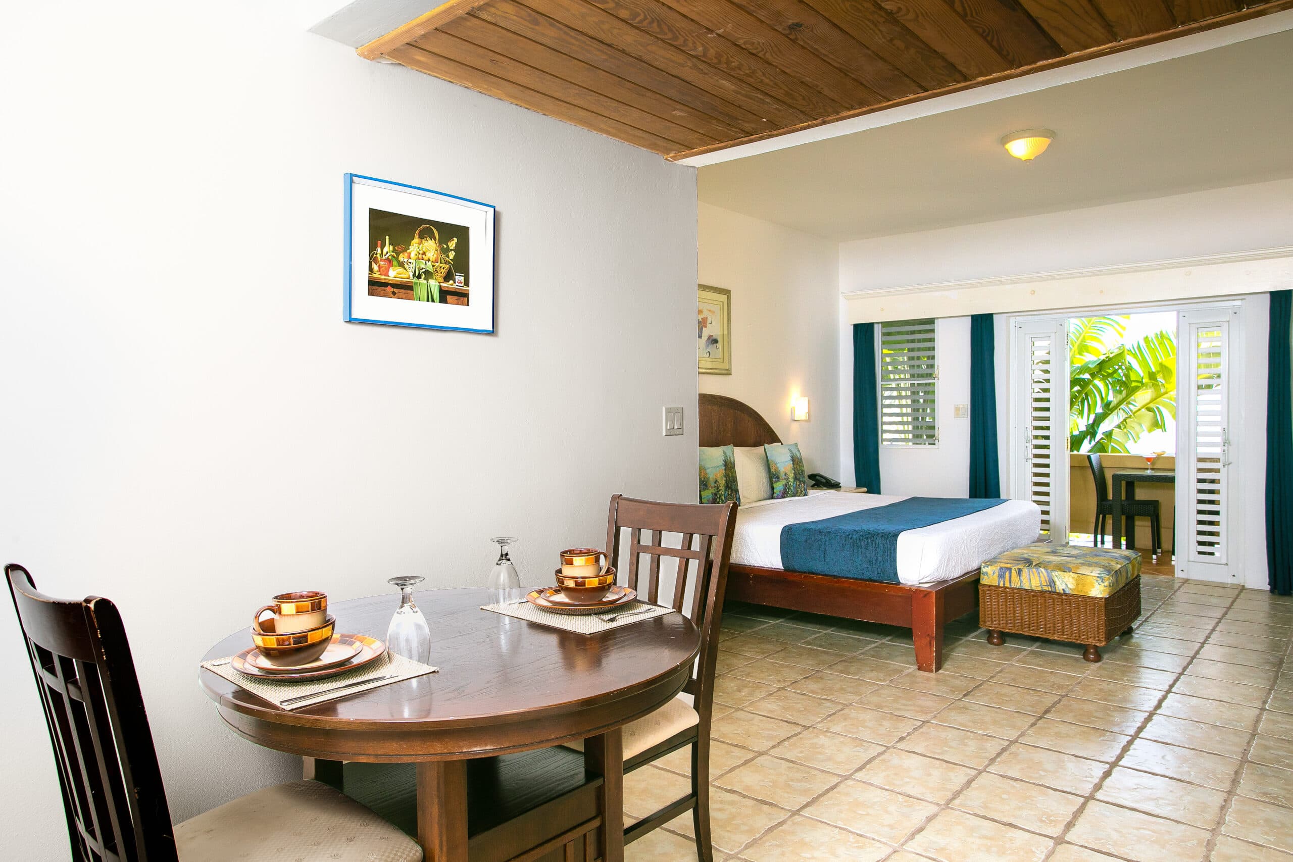 A cozy hotel room featuring a dining table, artwork, and a bed with views of a patio.