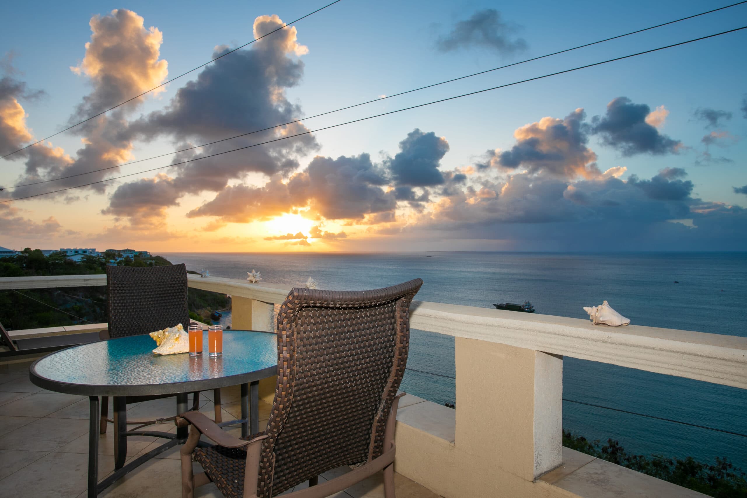 A serene sunset view over the ocean from a balcony with a table set for two.