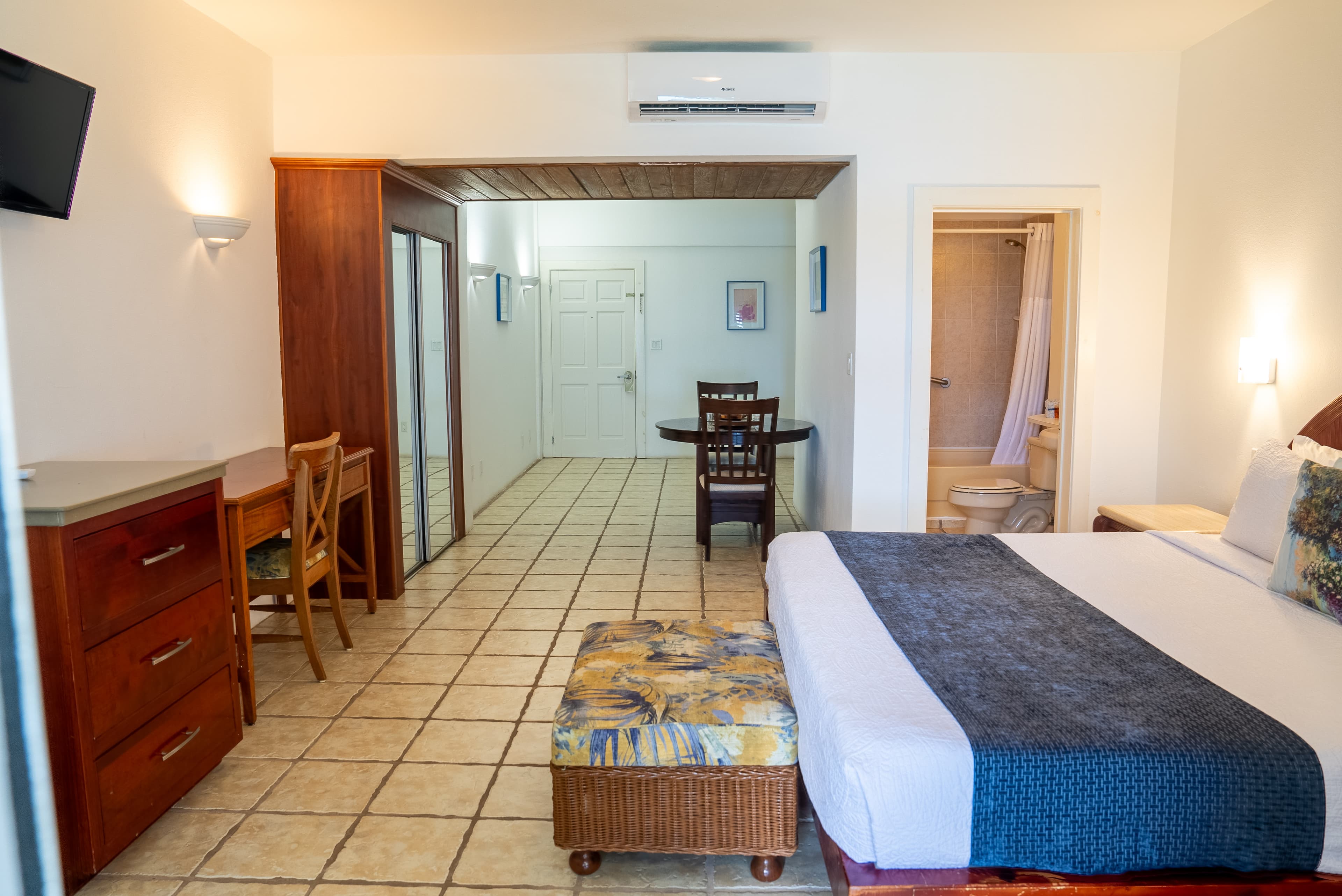 A spacious hotel room featuring a king-size bed, seating area, dining table, and a bathroom.