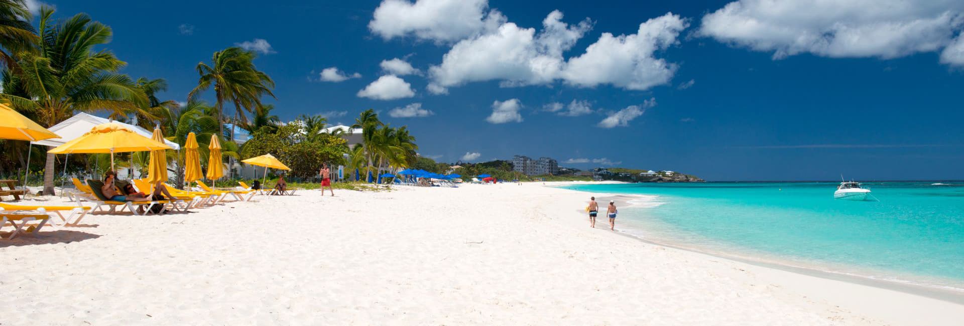 A serene beach scene with white sand, turquoise waters, palm trees, and people walking along the shore.