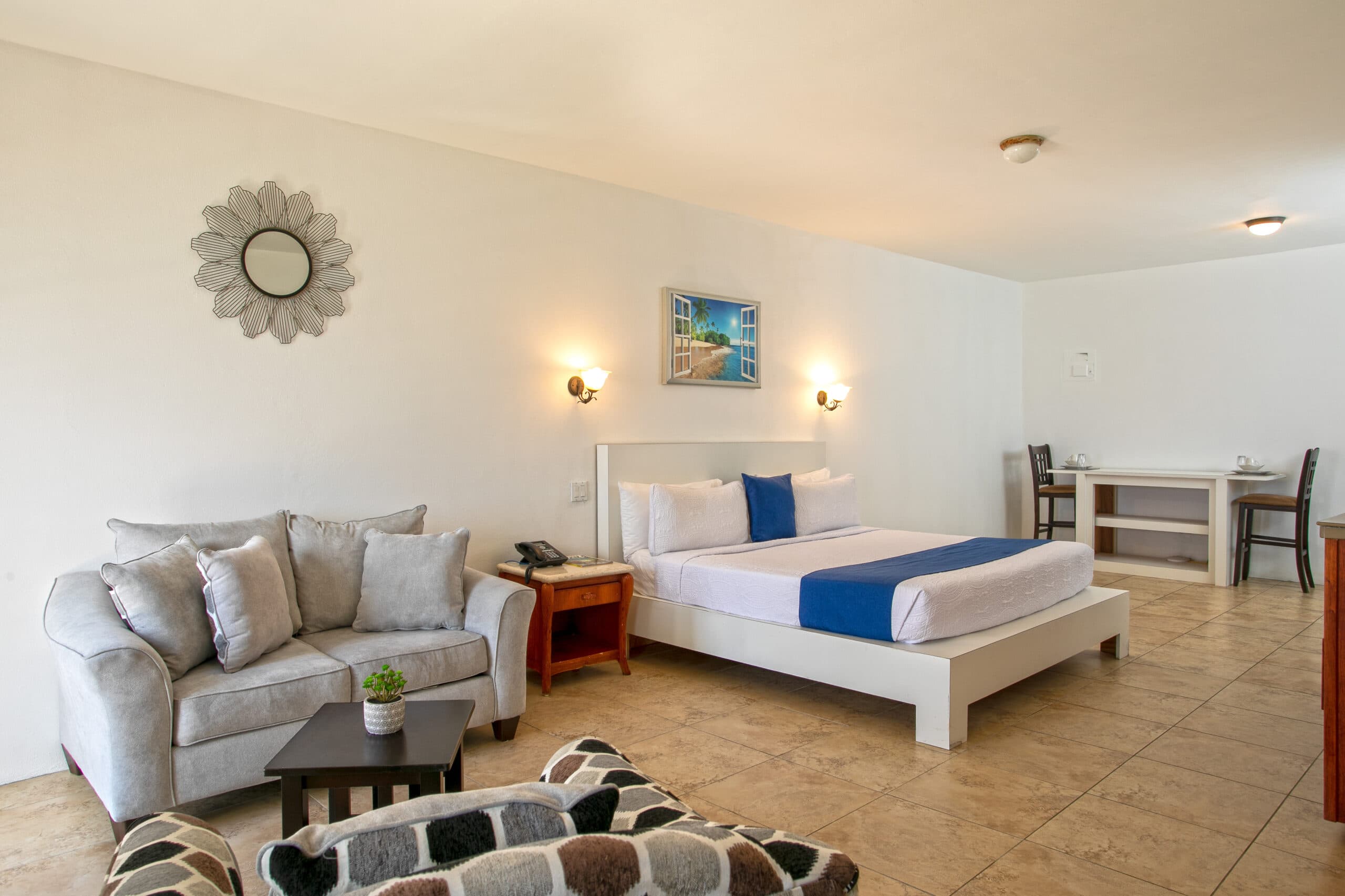 A stylish hotel room featuring a bed, sofa, and dining area with modern decor.