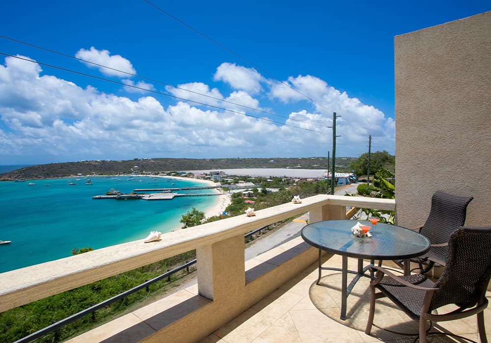 A balcony view overlooking a turquoise ocean and a sandy beach on a sunny day.